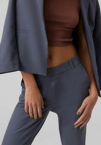 Mörkblå kostymjacka med vida ärmar, matchad med slimfit-byxor. Ovanpå bärs en brun ribbad croptopp. Texturen framstår som slät och skräddarsydd.