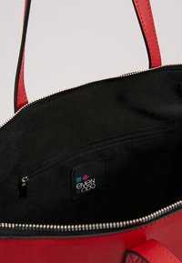 Červená kabelka s černým interiérem, uvnitř s kapsou na zip a viditelným štítkem značky "even & odd".