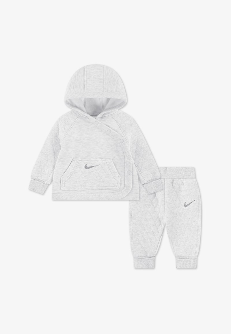 Svetlo siva trenirka s kapuco in hlače, z zapiranjem na zatiče, prešitim vzorcem in srebrnim logotipom Nike na obeh kosih.