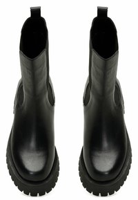 Botines negros de cuero con un acabado suave, que presentan paneles laterales elásticos, lengüetas para facilitar el calzado y una suela gruesa de goma con relieve.