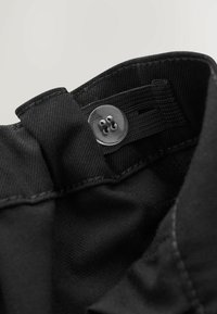 Czarna tkanina o fakturowanej powierzchni, z okrągłym, przezroczystym guzikiem i przeszyciem przy kołnierzu. Prosty i funkcjonalny design.