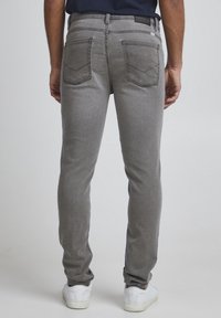 Szare jeansy z denimu o dopasowanym kroju, z dwoma tylnymi kieszeniami i kontrastującym przeszyciem, zestawione z białymi trampkami.