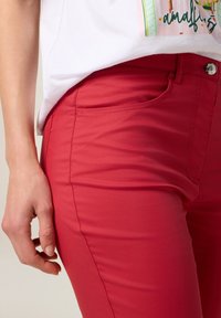 Pantalons ajustés rouges en tissu lisse, dotés d'une poche avant, d'une fermeture à bouton et de détails de surpiqûre subtils le long des côtés.