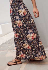 Zwiewna, granatowa długa spódnica w kwiaty z wyrazistymi różowymi, czerwonymi i białymi kwiatami. Wykonana z lekkiego materiału; posiada marszczoną talię i luźny krój.