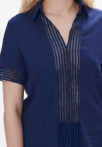Camicia di lino blu navy con collo, caratterizzata da dettagli in pizzo verticale lungo la parte anteriore e accenti in pizzo decorati sulle maniche.