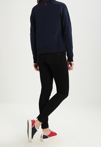 Sudadera navy con un detalle de corazón rojo en la parte posterior, combinada con jeans skinny negros y zapatillas rojas, blancas y navy.