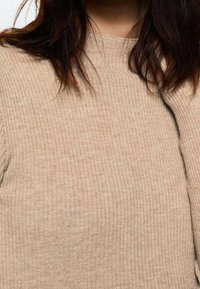 Pull côtelé beige avec col montant, présentant un motif en maille texturée et des détails de couture subtils sur la couture de l'épaule.