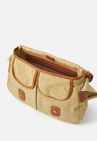 Beige canvas schoudertas met bruin leren accenten. Twee voorzakken, ritscompartiment binnenin, gestikte details en hardware in goudkleur.