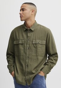 Olijfgroene button-up shirt van een gestructureerde stof met twee voorzakken, voorzien van bruine knopen en een klassieke kraagstijl.