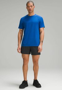 Blue athletic t-shirt with short sleeves and a crew neck, paired with black shorts. The fabric appears lightweight and moisture-wicking.