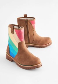 Las botas de tobillo de ante marrón presentan un zipper lateral y rayas de colores en rosa, azul y verde. Suela de goma texturizada con dibujo visible.