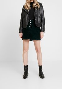 Black leather biker jacket over a black top, paired with a green corduroy skirt featuring silver buttons and ankle black boots.
