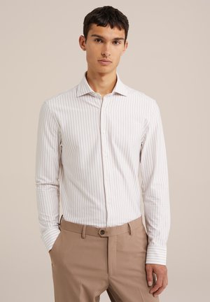 Camicia a righe bianca e beige con maniche lunghe, dotata di un colletto classico e realizzata in un tessuto leggero e morbido. I pantaloni sono beige.