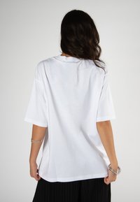 Biela krátkopsá t-shirt s okrúhlym výstrihom, vo voľnom strihu a hladkou látkou. Má jednoduchý chrbát bez vzorov alebo grafiky.