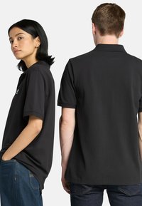 Černé polo tričko vyrobené z bavlněné směsi, s klasickým límcem, krátkými rukávy a logem na levé části hrudi. Ležérní design.