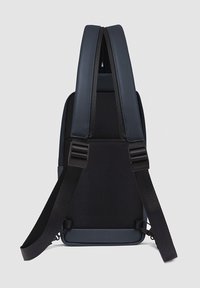 Zaino sottile in blu navy scuro, con schienale in mesh nero testurizzato, spallacci regolabili e cuciture rinforzate lungo le giunture.