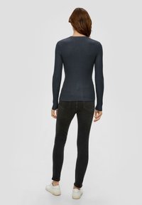 Dunkel gestreiftes Langarmoberteil mit tailliertem Design, kombiniert mit schwarzen Skinny-Jeans und weißen Sneakern. Strukturierter Stoff, runder Ausschnitt.