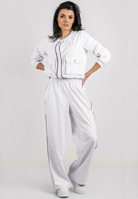 Completo tuta bianca composto da giacca con zip, due tasche frontali e polsini elasticizzati, abbinato a pantaloni a gamba larga, entrambi con dettagli neri.