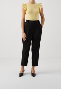 Geel geribbelde gebreide top met gerimpelde mouwen, gecombineerd met hoge zwarte broeken en zwarte puntige flats. Zachte texturen en een getailleerde pasvorm.