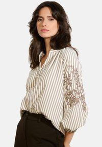 Blusa a righe in beige e marrone con design floreale ricamato sulle maniche. Caratterizzata da una chiusura con bottoni e una silhouette morbida.