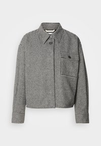 Houndstooth-patterned jacket in black and white, featuring a collar, front button closure, and a chest pocket with a button detail.