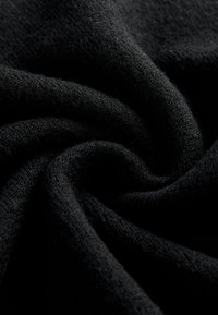 Tessuto nero con una superficie morbida e testurizzata, che mostra pieghe e grinze, indicativo di un materiale vellutato, ideale per calore e comfort.