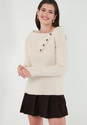 Cream-colored sweater with a wide ribbed cowl neck and button details. Soft texture, fitted sleeves, and a slightly cropped hem.