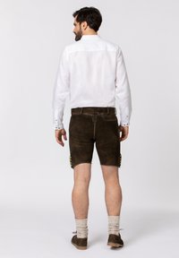 Braune Leder-Shorts mit einem körpernahen Schnitt, verziert mit grünen Steppnähten. Kombiniert mit einem weißen Leinenhemd und beigen Socken.