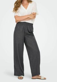 Šedé, volné lněné kalhoty s elastickým pasem, kombinované s bílým vrškem s výstřihem do V, který má na rukávech detaily z krajky.