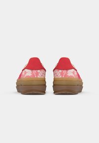 Red and pink floral print slip-on shoes with a textured upper, padded collar, and chunky brown rubber sole. Smooth and cushioned finish.