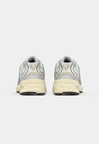 Een paar witte en beige mesh hardloopschoenen gezien vanuit de achterkant op een simpele witte achtergrond.