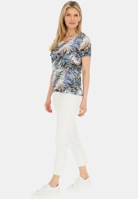 Koszulka z krótkim rękawem w kolorowym wzorze liści palmowych w odcieniach niebieskiego i beżowego; zestawiona z białymi spodniami typu cropped i białymi sneakersami.