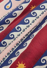 Tissu avec des rayures rouges, bleues et roses présentant des motifs tourbillonnants bleus, de petites formes paisley et des motifs solaires jaunes.