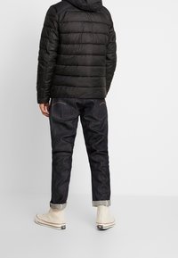 Svart pufferjacka med horisontella sömmar, bärs över mörk denimjeans. Beiga hög-top sneakers med röda accenter och uppvikta ärmar.