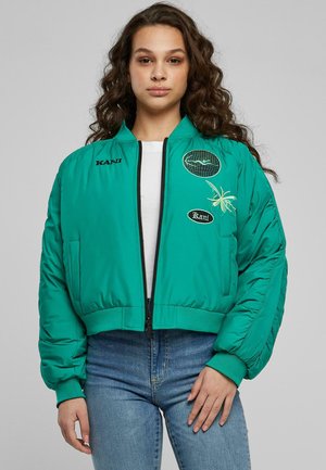 Grön bomberjacka med en kortad design, har broderade lappar, dragkedjestängning och ribbade manschetter. Slät textur, tillverkad av syntetiskt material.