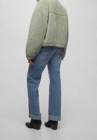 Grøn fleecejakke med en struktureret overflade, parret med lyseblå lige ben jeans og sorte hælede ankelstøvler.