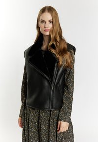 Zwarte leren bodywarmer met een brede kraag en ritssluiting, aangevuld met een lange jurk met bloemenpatroon. Glad materiaal en een getailleerde pasvorm.