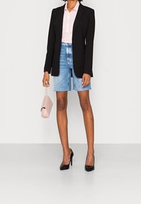 Černý blazer, světle růžová košile na knoflíky, světlé modré džíny šortky, černé vysoké podpatky a malá růžová kabelka. Jednoduchý, strukturovaný outfit.