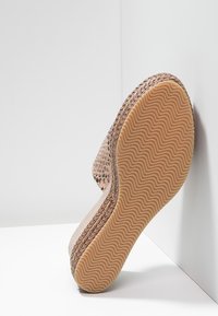 Beige espadrille med en texturerad skinnmönstrad ovandel, flätad jutekanter och en gummisula med ett vågmönstrat mönster.