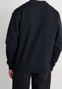 Black sweatshirt with a crew neckline, long sleeves, and ribbed cuffs. Soft texture and relaxed fit, paired with dark jeans.