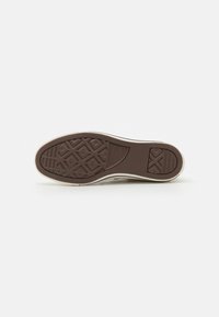 Brown rubber shoe sole with textured grip pattern, featuring a pronounced heel and a slight curve at the toe. Light-colored edging.