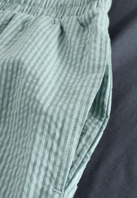 Tissu rayé vert clair avec une texture douce et une taille élastique froncée, présenté à côté d'un matériau gris foncé.