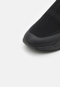 Black athletic shoe featuring a textured knit upper, rubber toe cap, and chunky sole for added grip and support.