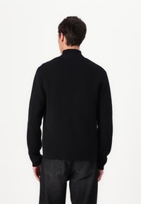 Black knit sweater with a high collar, long sleeves, and a smooth texture. Paired with dark denim jeans, viewed from the back.