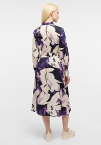 Abito midi floreale in tessuto viola, nero e crema; presenta maniche lunghe, una vita con cintura e una silhouette fluida con una texture morbida.
