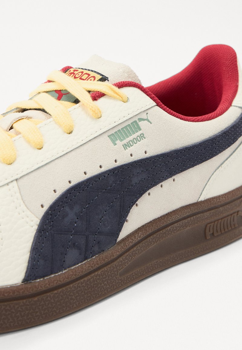 Białe skórzane sneakersy z granatowymi zamszowymi akcentami, żółtymi sznurówkami i czerwonym wnętrzem. Posiadają teksturowany wzór i wyraźne logo Puma.