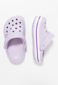 Ljuslila träskor med ventilationshål, en tjock vit sula, lila rand som accent, ett rem och ett präglat logotyp på fotbädden.