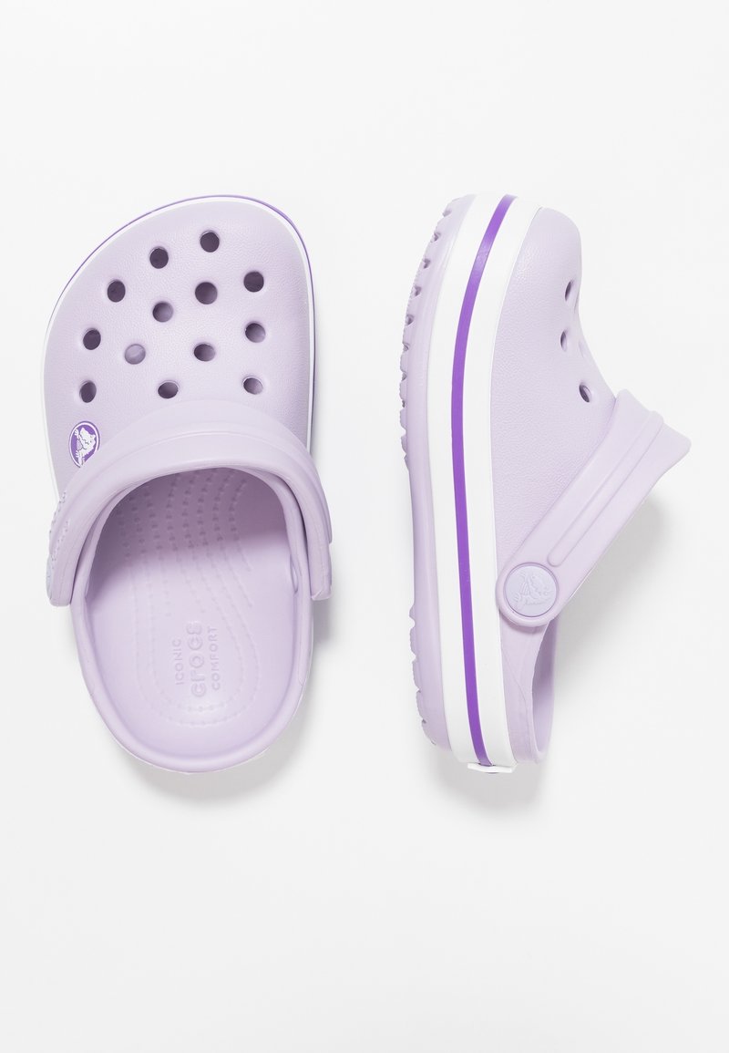 Ljuslila träskor med ventilationshål, en tjock vit sula, lila rand som accent, ett rem och ett präglat logotyp på fotbädden.