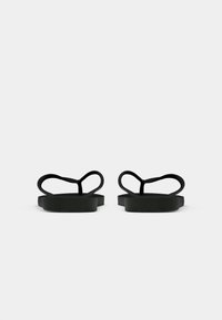Une paire de tongs noires simples avec des lanières en thong, vues de l'arrière sur un fond blanc unicolore.