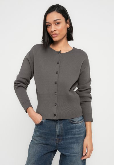 Cardigan en tricot gris foncé avec col rond, boutons à l'avant et poignets côtelés. Porté sur un jean en denim bleu.